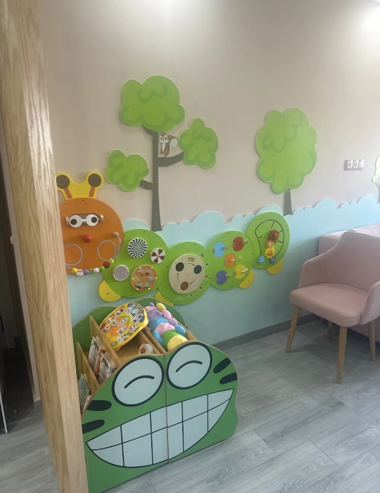 Coin jeux de la salle d'attente, avec un mur d'activités et une bibliothèque en forme de grenouille